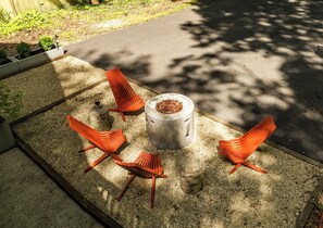 A concrete fire pit with a metal bowl in the center, surrounded by four orange chairs. - Modern A-frame cabin retreat in the woods of Middletown (Middletown)
