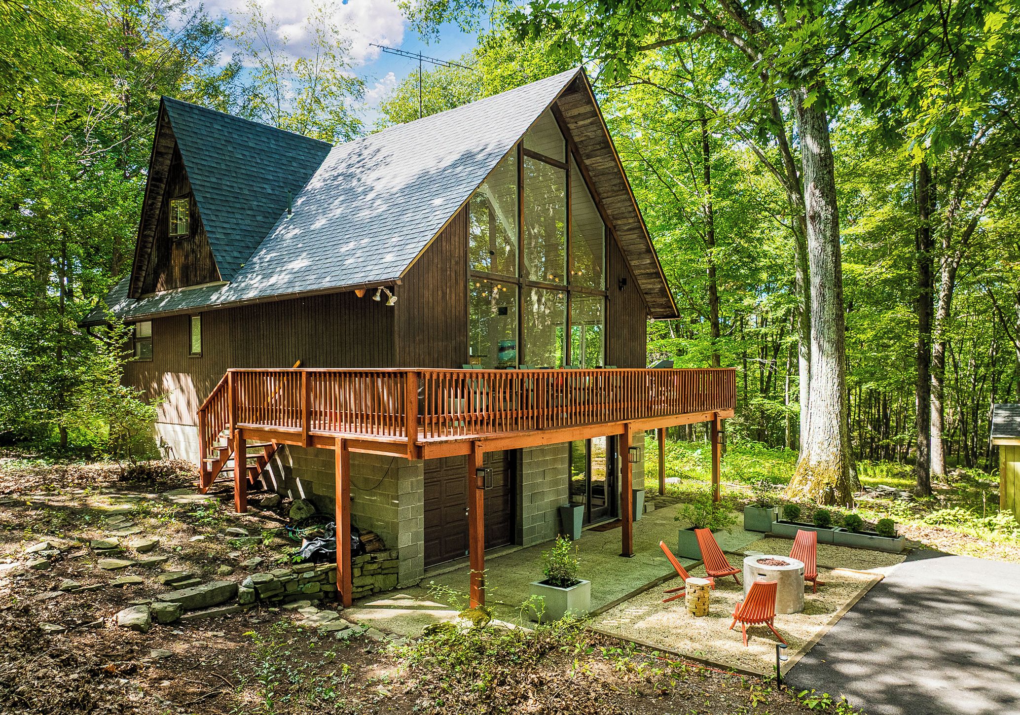 A wooden cabin with a glass extension, surrounded by trees.