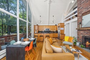 A spacious living area with a large sofa, dining table, and chairs, a kitchen with wooden cabinets, and a fireplace. - Modern A-frame cabin retreat in the woods of Middletown (Middletown)
