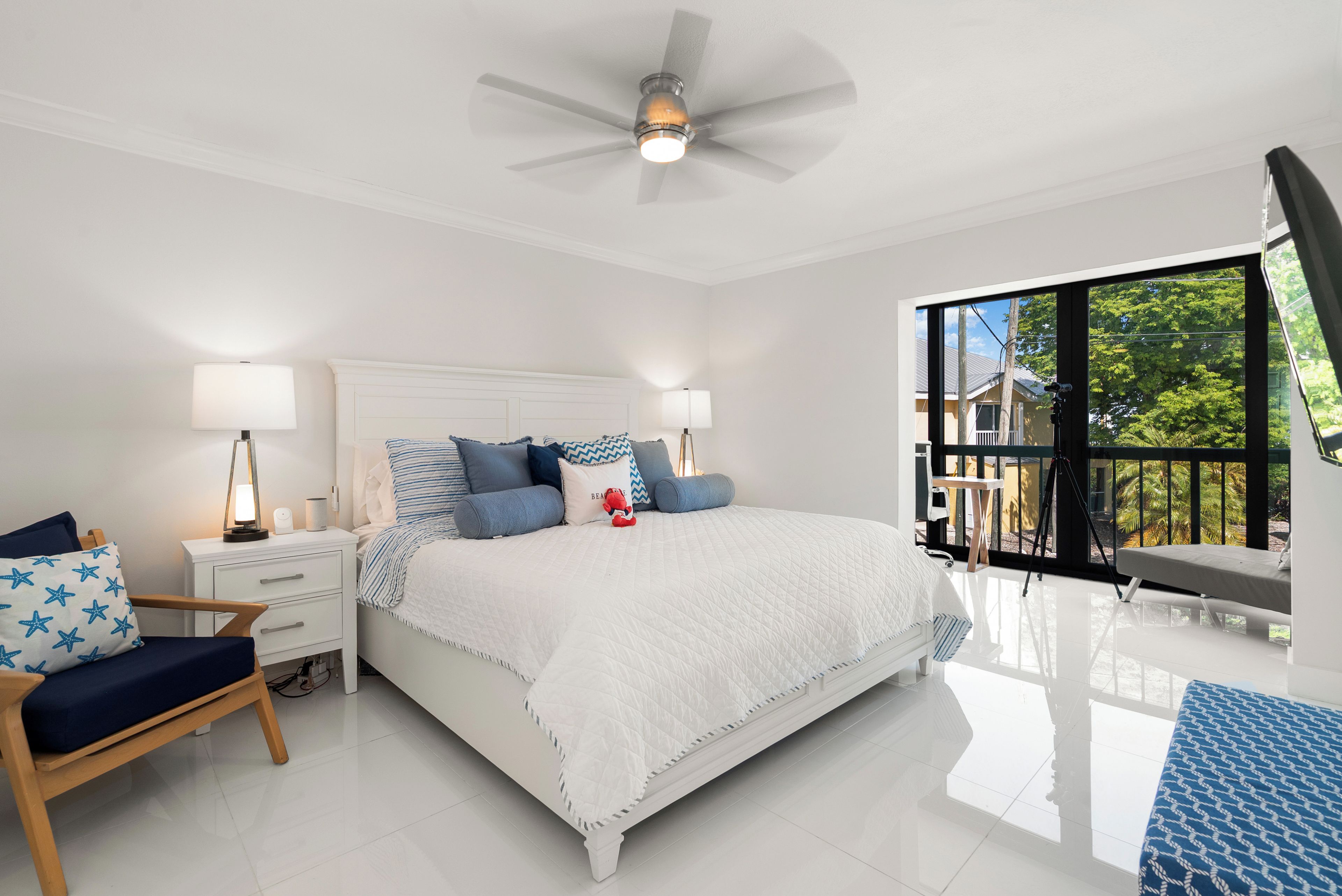 Une chambre à coucher comprenant un lit, des tables de chevet, une chaise, un ventilateur de plafond et un balcon avec vue.