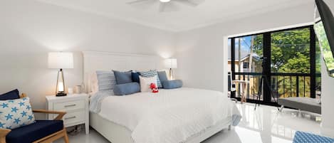 Un dormitorio con cama, mesitas de noche, una silla, ventilador de techo y balcón con vistas.