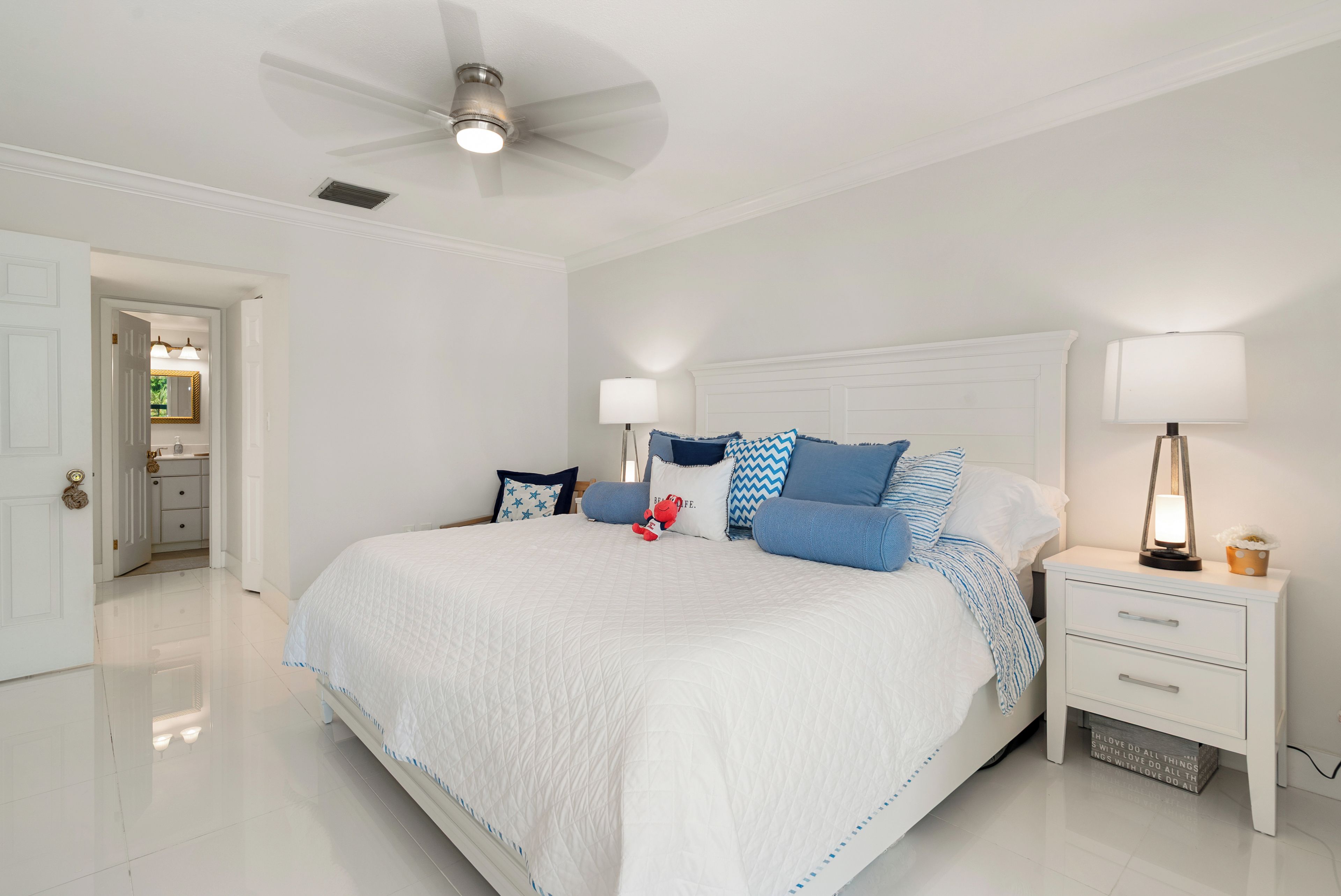 A spacious bedroom with a large bed, two bedside tables, a ceiling fan, and a nightstand with a lamp.