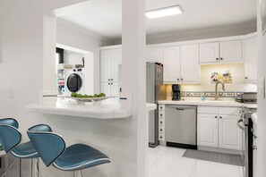 A modern kitchen with white cabinetry, a built-in dishwasher, and a countertop with a sink and a coffee maker. - Charming 2-bed 2bath townhome in gorgeous Key Largo perfect monthly winter stay. (Key Largo)