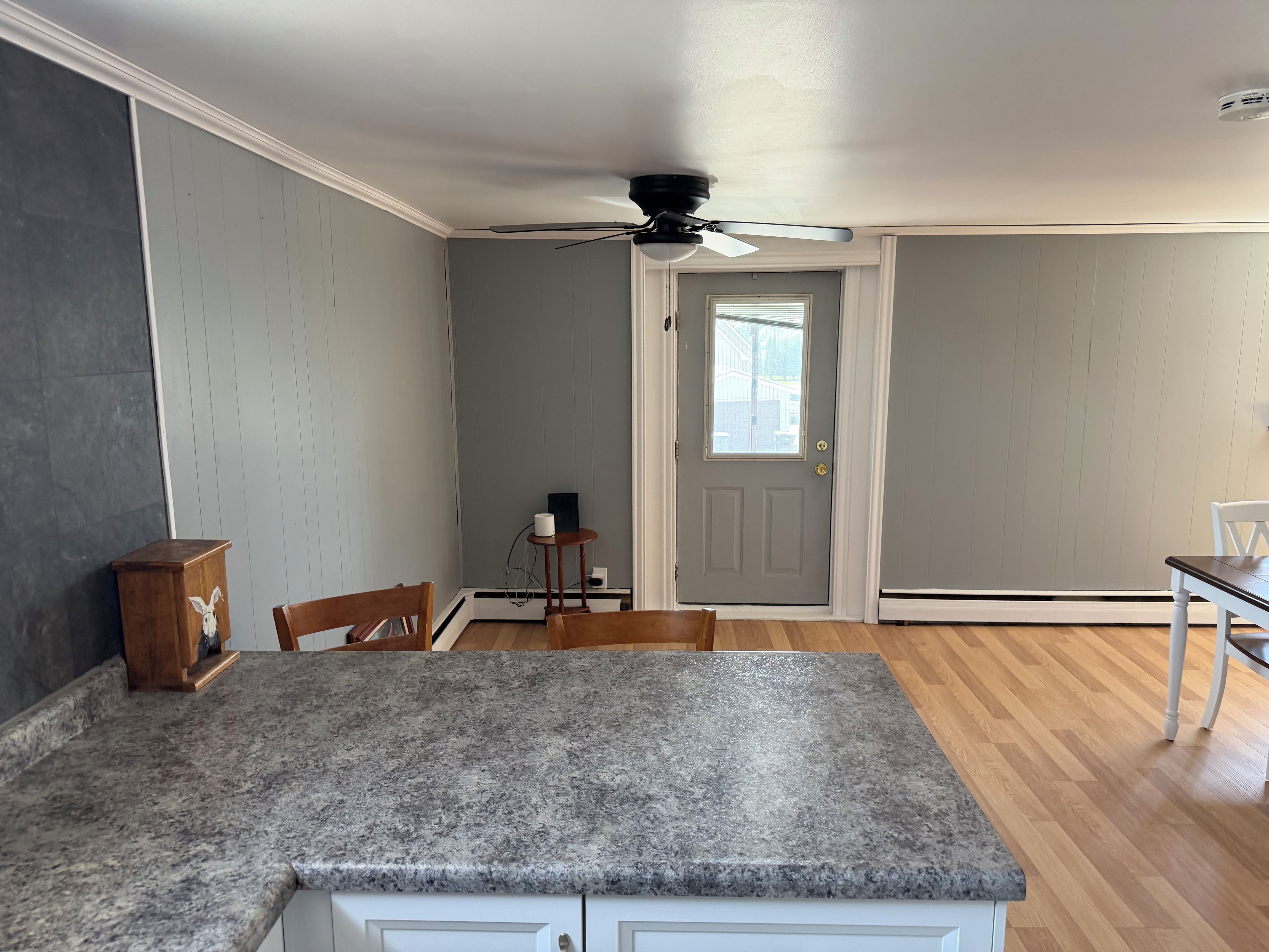 A kitchen with a granite countertop, wooden chairs, a ceiling fan, and a door with a window.