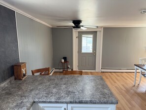 Une cuisine dotée d’un plan de travail en granit, de chaises en bois, d’un ventilateur de plafond et d’une porte avec une fenêtre.