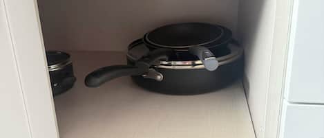 A kitchen cabinet with two black pots and a frying pan.