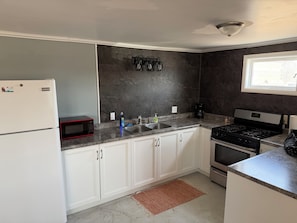 A kitchen with white cabinets, a stainless steel sink, a microwave, a stove, and a refrigerator.