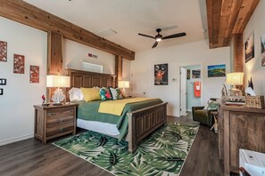 A bedroom with a bed, wooden headboard, nightstands, a ceiling fan, and a tropical-themed rug. - Shore Dream-Game Room/Community Pool/Mins to Beach (Port Aransas)