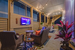 A room with wicker furniture, a flat-screen TV, and a staircase. - Shore Dream-Game Room/Community Pool/Mins to Beach (Port Aransas)