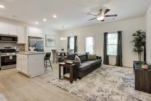 A modern kitchen with white cabinetry, a built-in island, and a dining area with a gray sofa and a small table.