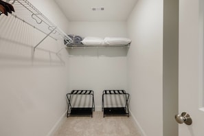 A small, enclosed room with a bunk bed, a metal shelf with folded clothes, and a door with a round handle.