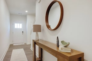 Un couloir avec une console en bois, un miroir fixé au mur, un lampadaire et une porte au fond.