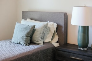A bed with a quilted cover, two pillows, a bedside table with a lamp, and a drawer.