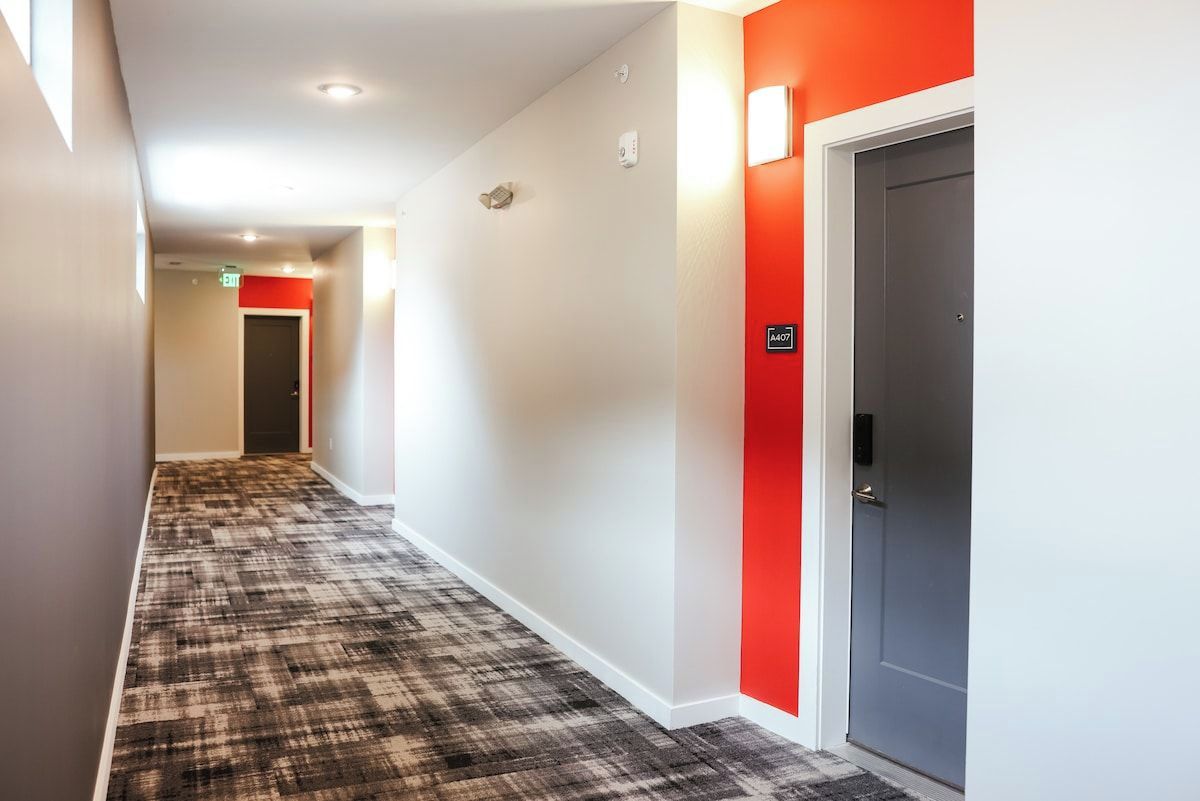 Ein Hotelgang mit einem gemusterten Teppich, einer roten Akzentwand und einer Tür mit einem Schild.