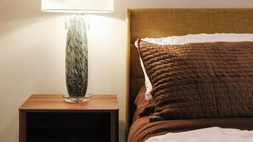 A neatly made bed with a brown quilt, a wooden nightstand with a lamp, and a drawer.
