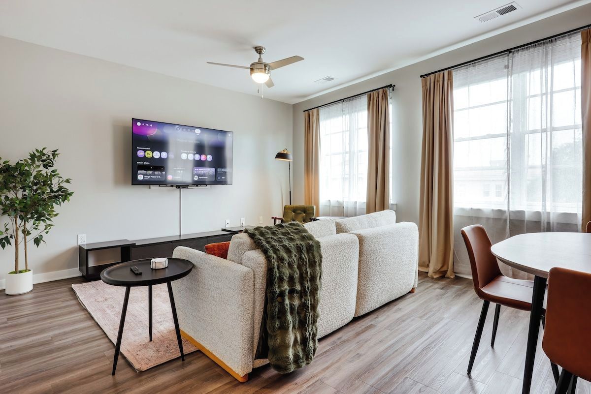 Ein modernes Wohnzimmer mit Flachbildfernseher, Deckenventilator, Sofa, Esstisch und einer Topfpflanze.
