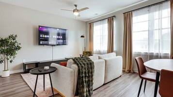 Ein modernes Wohnzimmer mit Flachbildfernseher, Deckenventilator, Sofa, Esstisch und einer Topfpflanze.