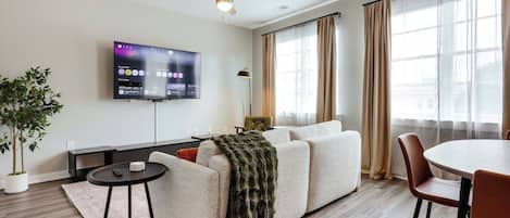 En moderne stue med et fladskærms-tv, en loftsvifter, en sofa, et spisebord og en potteplante.