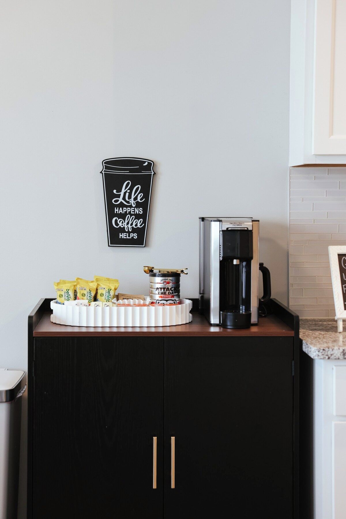 A kitchen counter with a coffee maker, a coffee cup, and a tray of coffee pods.