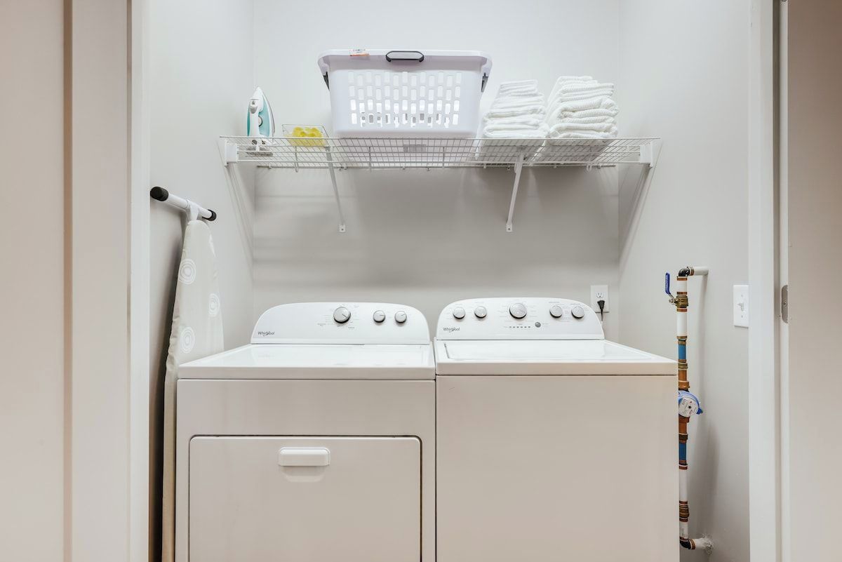 A laundry area with two stacked washers and dryers, a basket, and a shelf with folded towels.