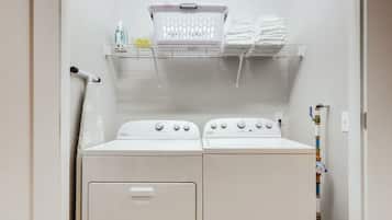 A laundry area with two stacked washers and dryers, a basket, and a shelf with folded towels.