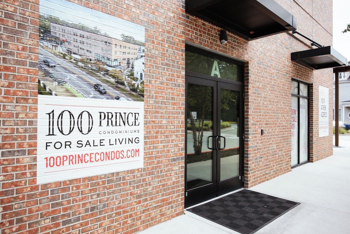 A brick building with a glass door entrance and a sign advertising 100 Prince condominiums for sale.