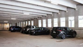 A parking garage with concrete pillars, overhead lighting, and large windows.
