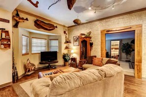 A cozy living room with a large sofa, a flat-screen TV, and a fireplace. - 43-Acre Cabin Retreat with Pond, Hot Tub & Windrock Park Trail Access (Oliver Springs)