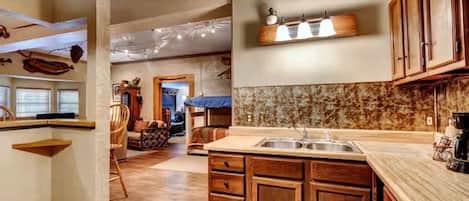 Una cocina con armarios de madera, un fregadero y una encimera. Hay una zona de comedor con una silla y una mesa.