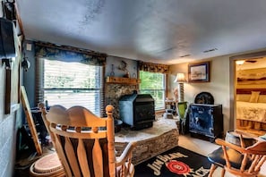 A rustic interior with a stone fireplace, wooden furniture, and a view of the outdoors. - 43-Acre Cabin Retreat with Pond, Hot Tub & Windrock Park Trail Access (Oliver Springs)