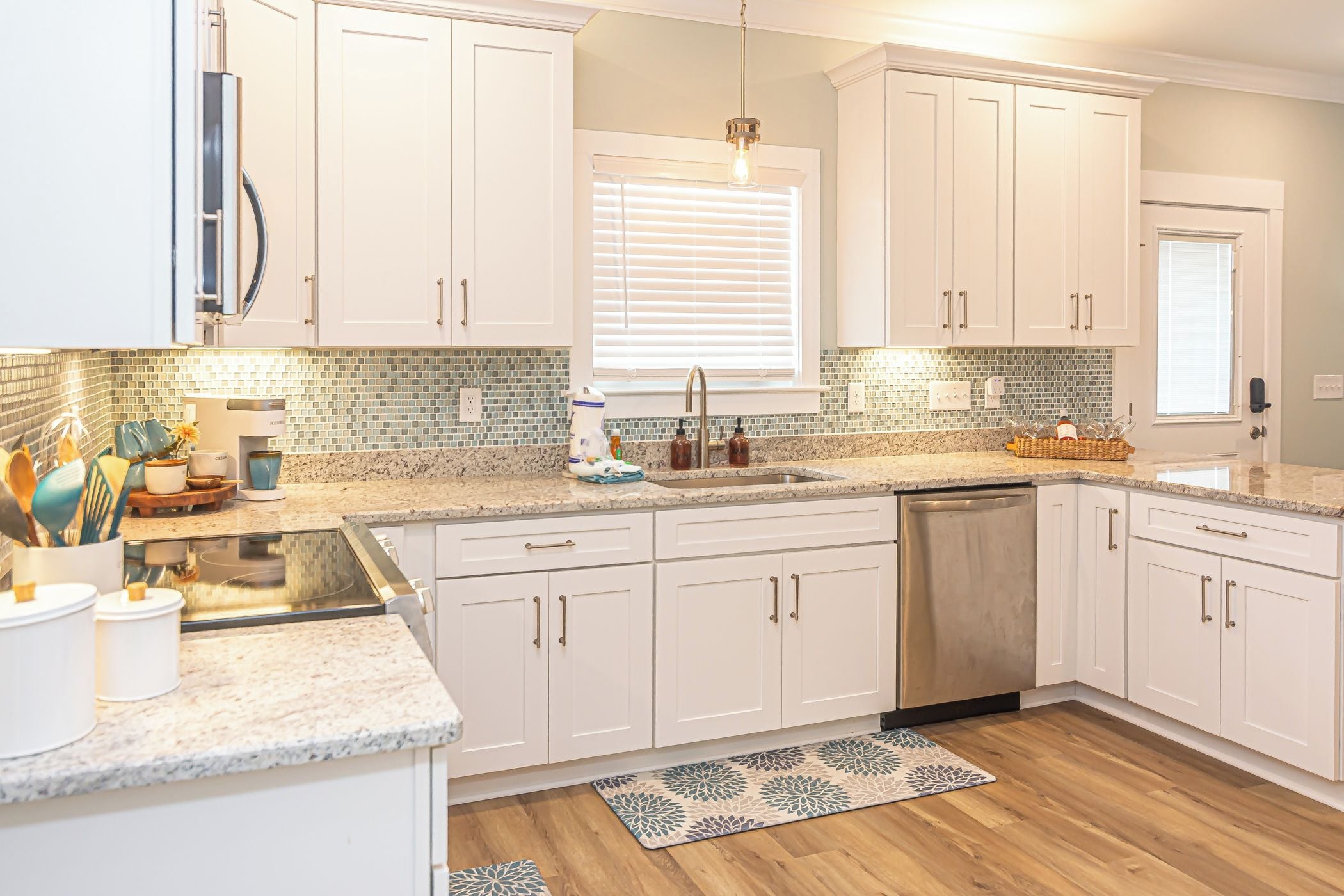 A kitchen with white cabinets, a granite countertop, a built-in dishwasher, and a window with blinds.