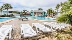 Piscina com espreguiçadeiras e mesa de piquenique, cercada por palmeiras e edifícios.