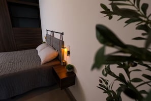 Un dormitorio con cama, mesita de noche, lámpara y una planta en maceta.