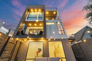 Een modern meerlaags gebouw met balkon, grote ramen en lichtslingers.