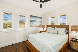 Ein Schlafzimmer mit einem großen Bett, zwei Nachttischen, einem Deckenventilator und Fenstern mit Jalousien.