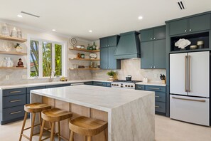 A modern kitchen with a central island, bar stools, and a large refrigerator. - Poipu Luxury Retreat, Sleeps 14, Walk to the beach, Pool, AC + Ohana (Koloa)