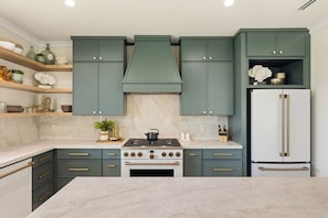 Een keuken met blauwgroene kastjes, een witte koelkast en een centraal geplaatst fornuis.