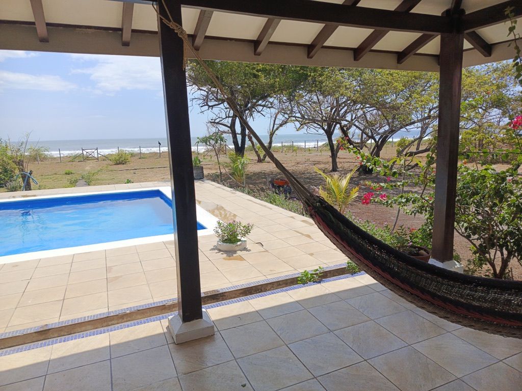 A covered outdoor area with a swimming pool, a hammock, and a view of the beach.