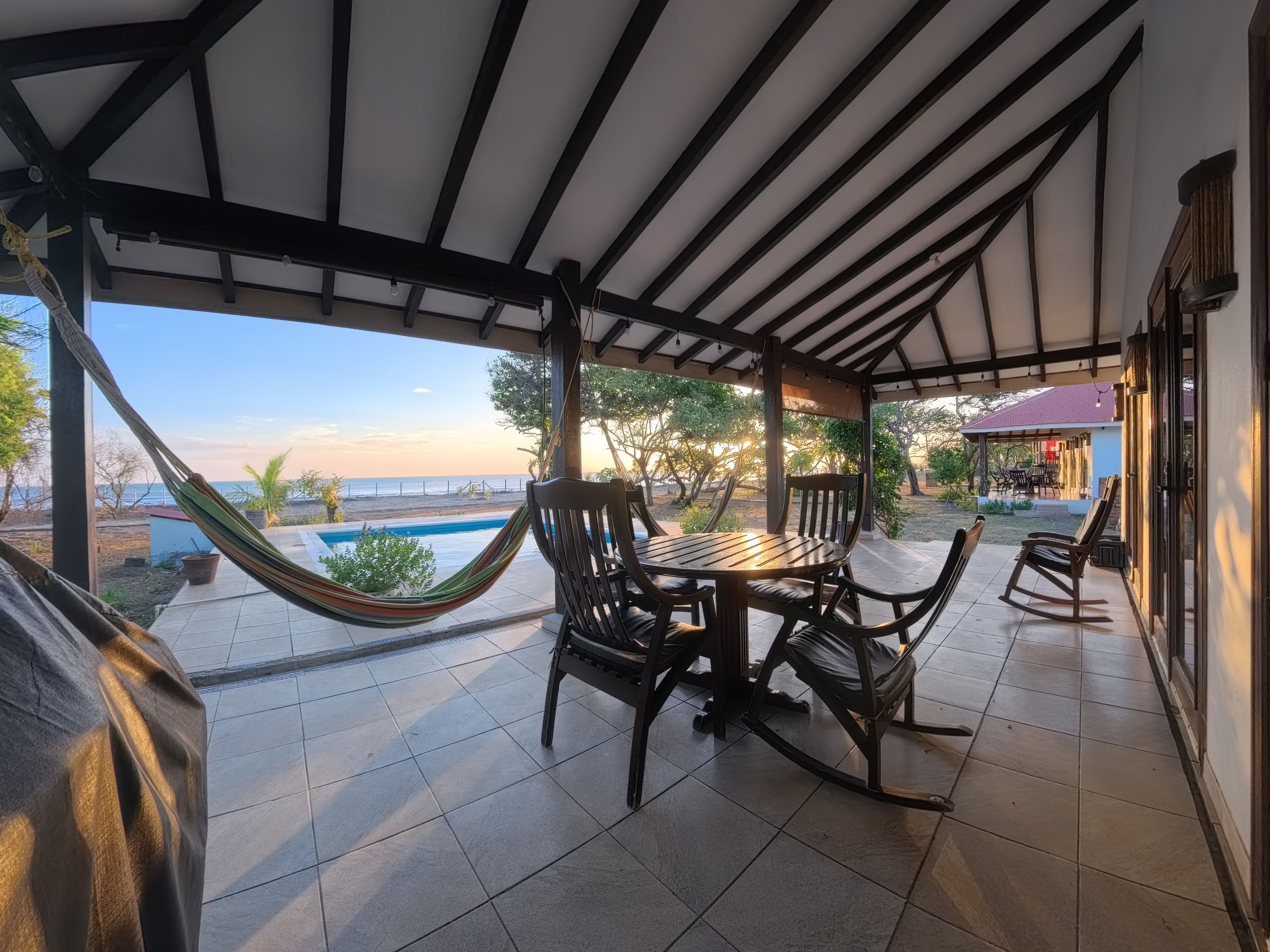 Un patio techado con piscina, mobiliario exterior y vista a la playa.