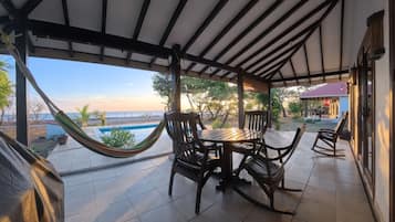 Un patio techado con piscina, mobiliario exterior y vista a la playa.
