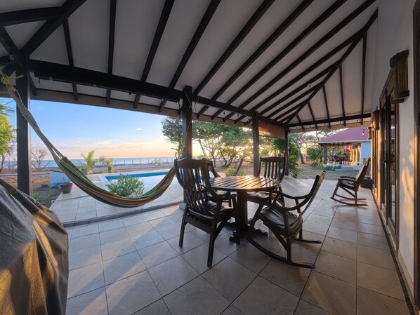 A covered patio with a pool, outdoor furniture, and a view of the beach.