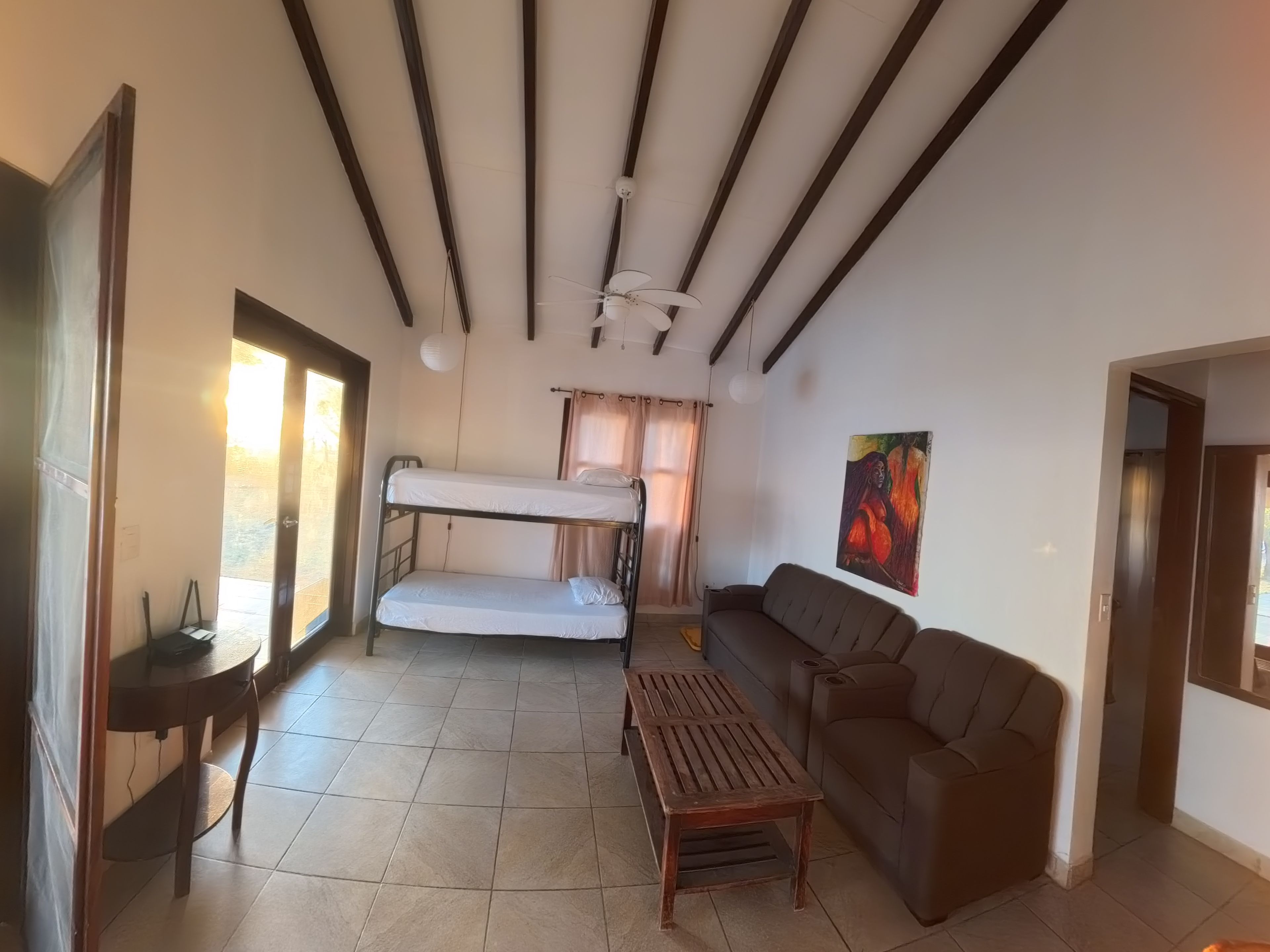 Una habitación con una cama litera, un sofá, una mesita y un ventilador de techo.
