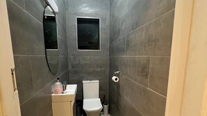 Un baño estrecho con baldosas grises, un inodoro, un lavamanos, un espejo y una pequeña ventana.