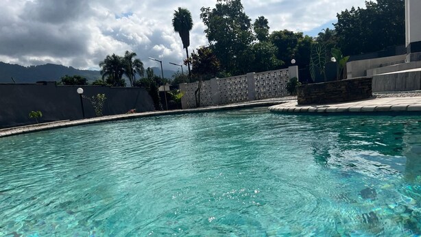Una piscina cristalina con base de azulejos, rodeada por un bajo muro de piedra y un borde de concreto.