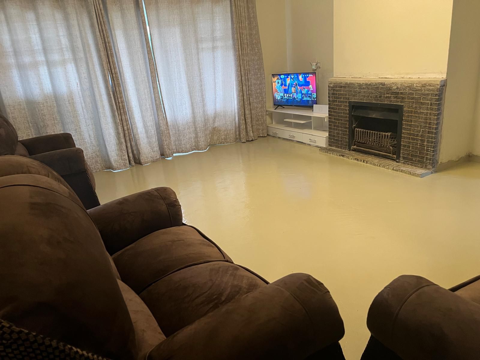 Ein Wohnzimmer mit Flachbildfernseher auf einem Standfuß, Kamin und einer großen braunen Couch.