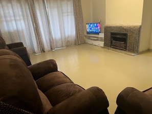 A living room with a flat-screen TV on a stand, a fireplace, and a large brown sofa.