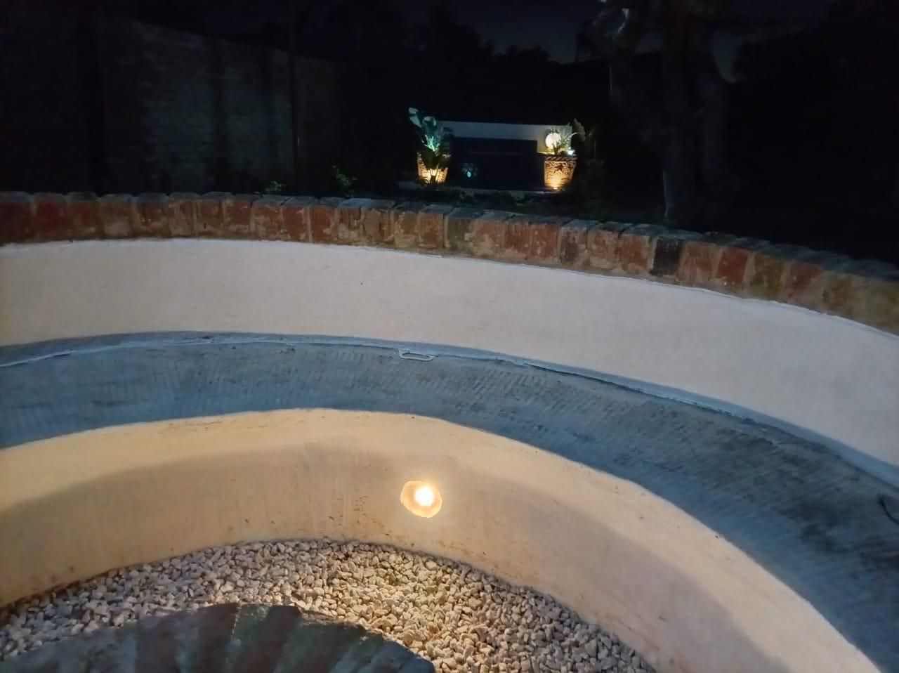 Un espacio de estar al aire libre con forma circular, con una fuente de luz central rodeada por un muro de ladrillo bajo.