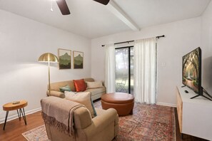 Una sala de estar moderna con sofá, sillón, reposapiés, lámpara de pie y televisor de pantalla plana.
