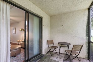 A balcony with a glass door leading to a room, two chairs, and a small table.