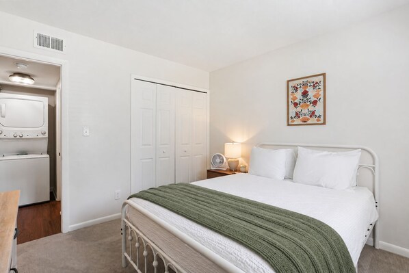 A bedroom with a bed, a nightstand, a lamp, a fan, and a wardrobe.
